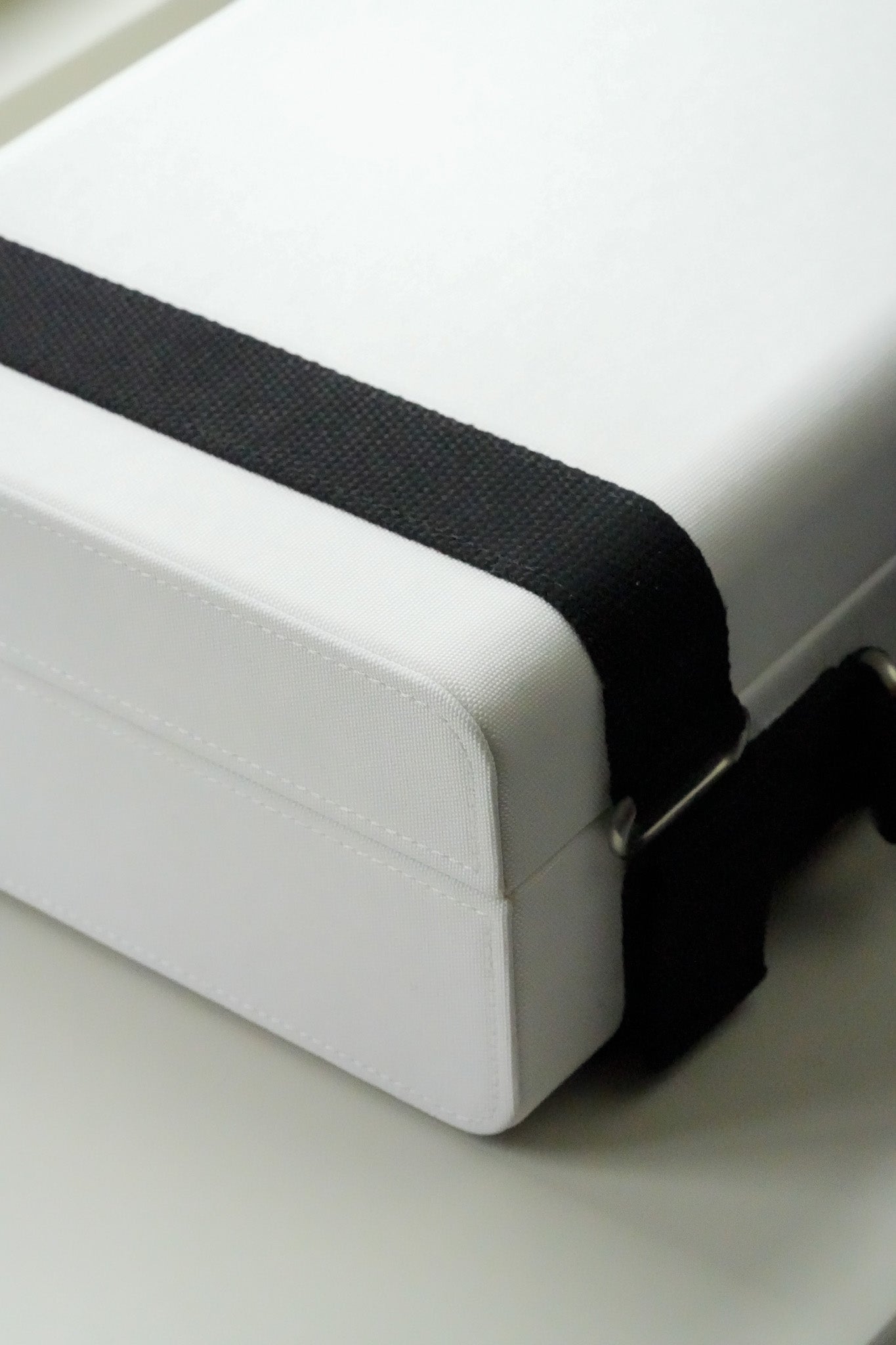 White box with a black strap on a light gray background