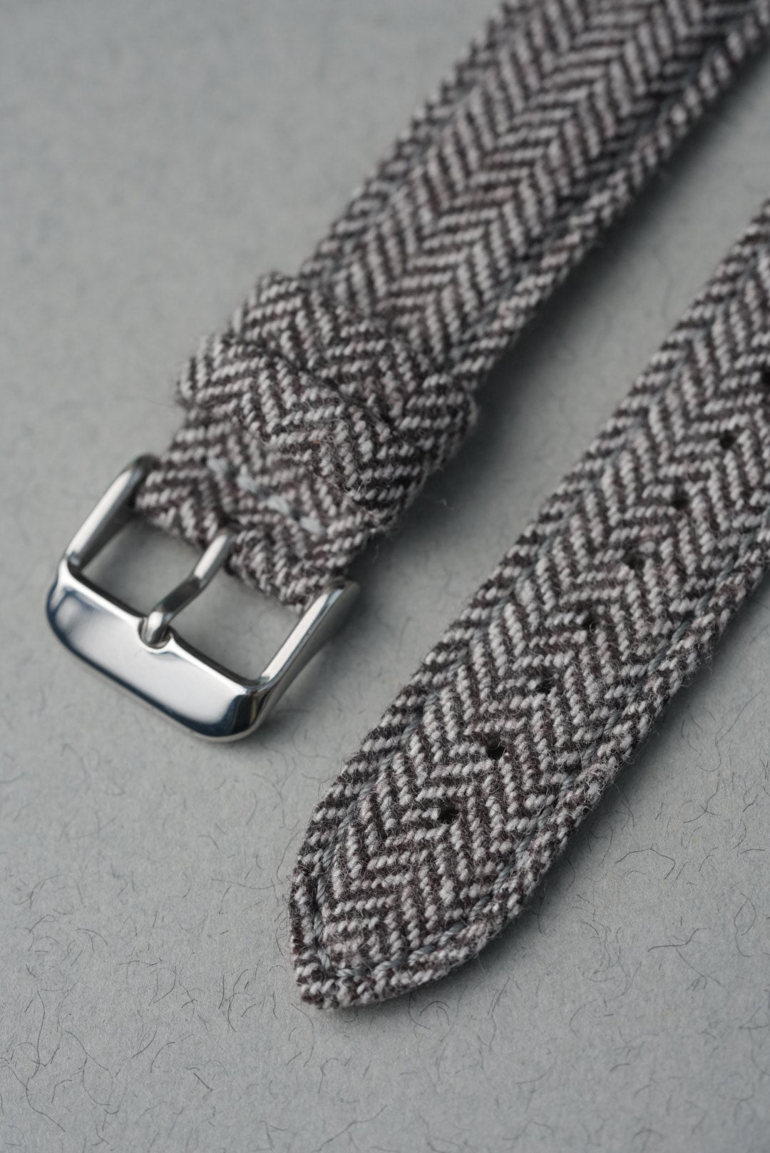 Gray herringbone patterned belt with a silver buckle on a gray background
