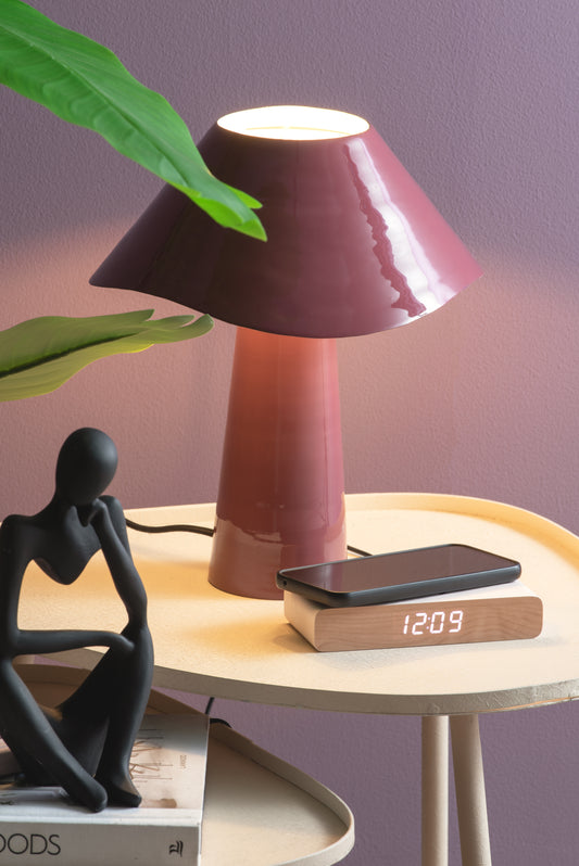 Table lamp on a small round table with a smartphone displaying the time, a figurine, and a plant.