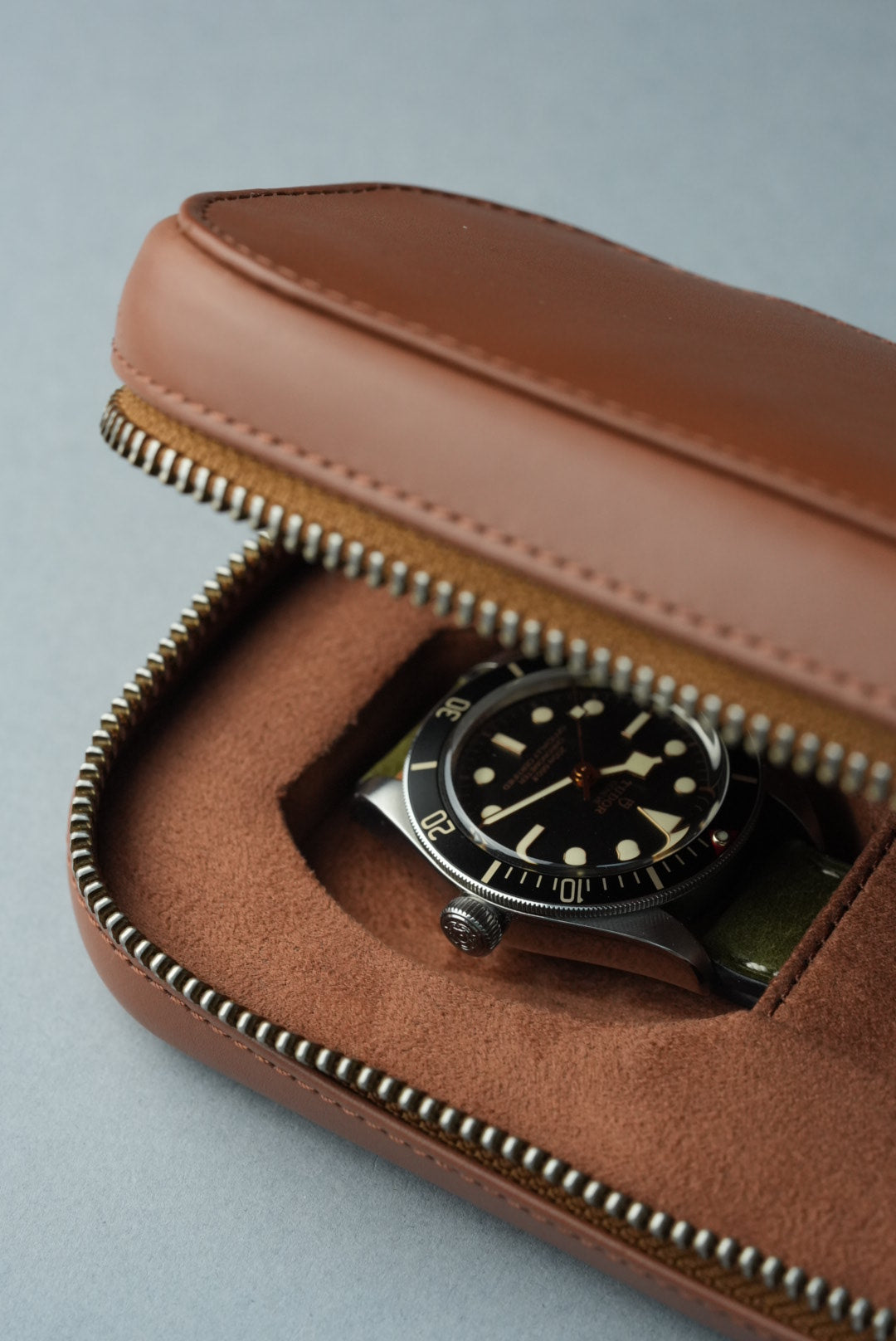 Brown leather case with a vintage watch inside on a light gray background
