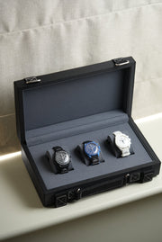 Black watch box with three watches on a light gray surface