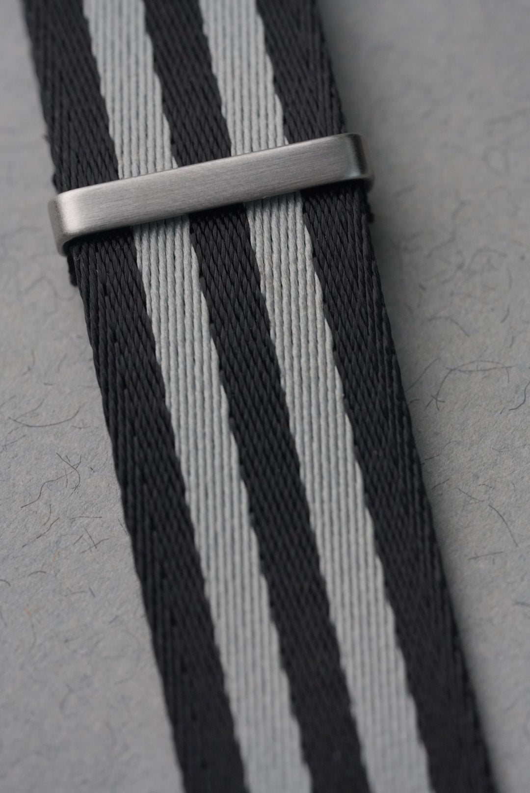 Nato strap with black and gray stripes and a silver buckle on a gray background