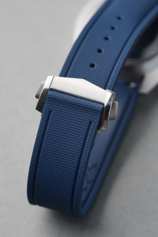 Close-up of a blue watch strap with a silver buckle on a gray background