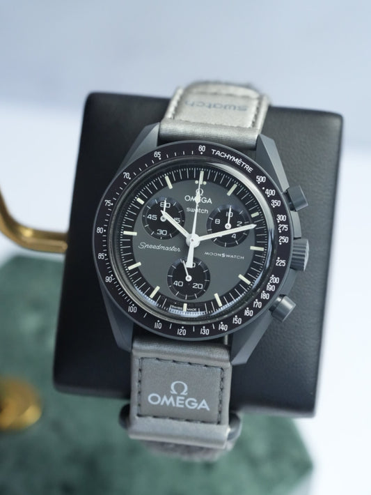 A Swatch x OMEGA MoonSwatch Collection watch with a deep grey dial, metallic VELCRO strap, and white chronograph hands.