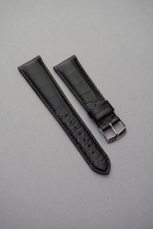 Black alligator embossed leather watch strap laid flat with polished stainless buckle