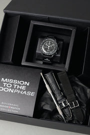 Black Snoopy MoonSwatch gift set in box with watch, alligator leather strap, suede strap, and spring bar tool.