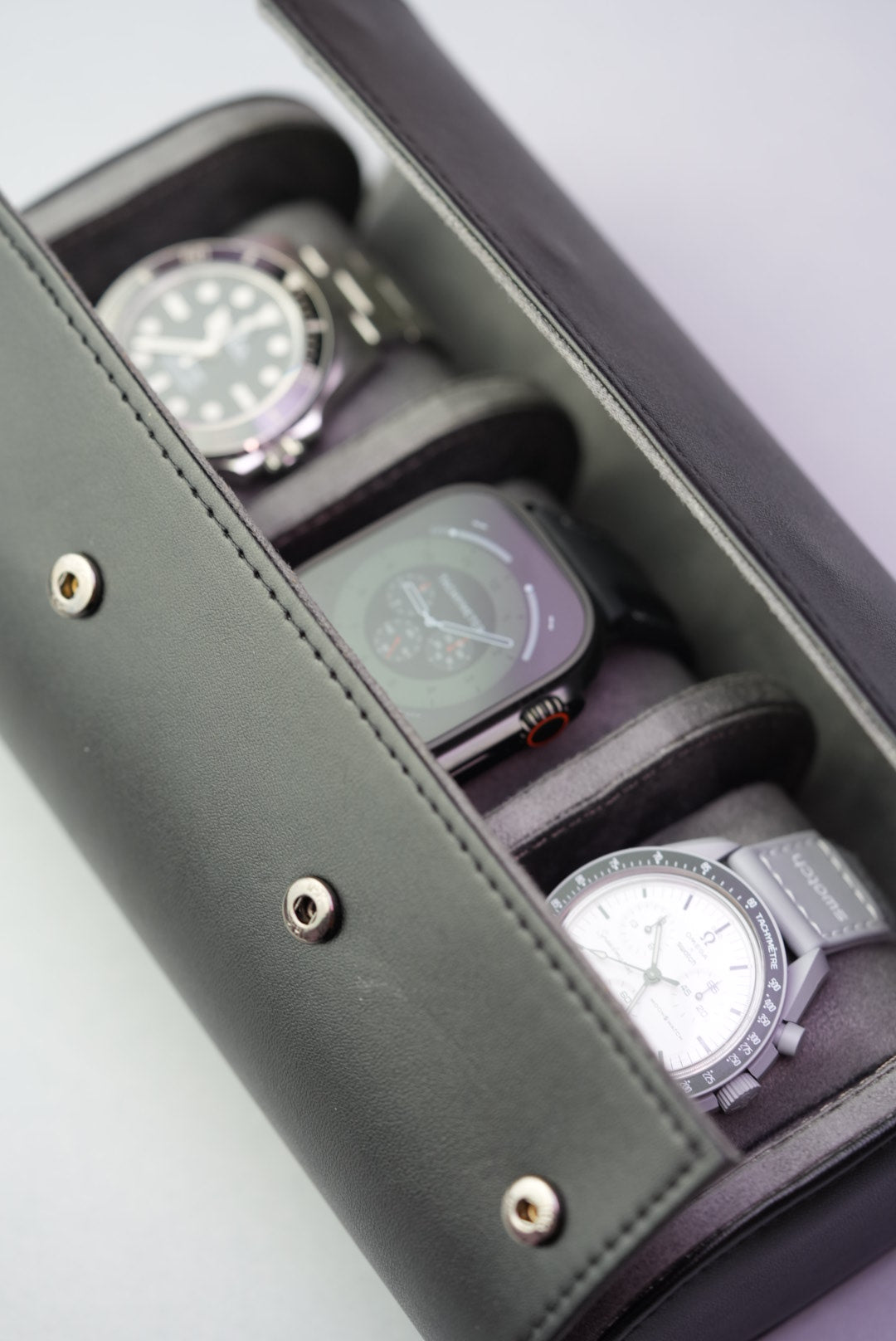 Open black watch roll holding three watches including Rolex, Apple Watch Ultra, and Omega Speedmaster.