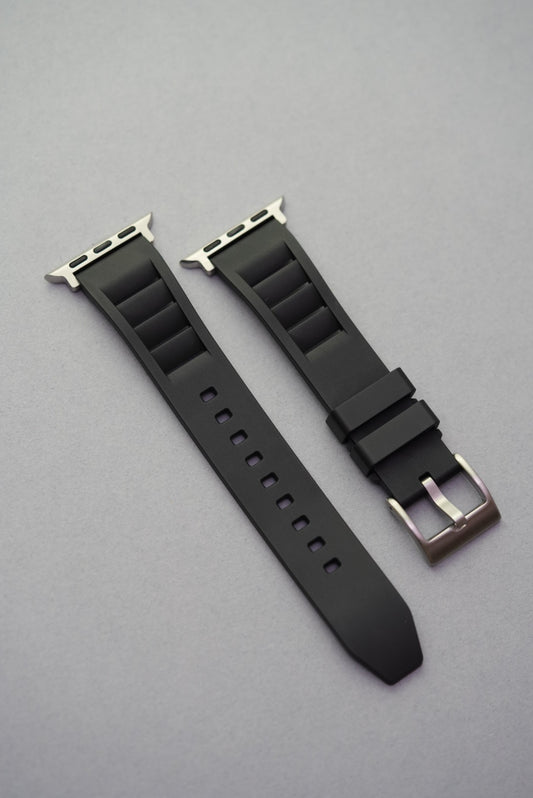 Black vented FKM rubber strap with Apple Watch adapters and brushed buckle, laid flat for product display.