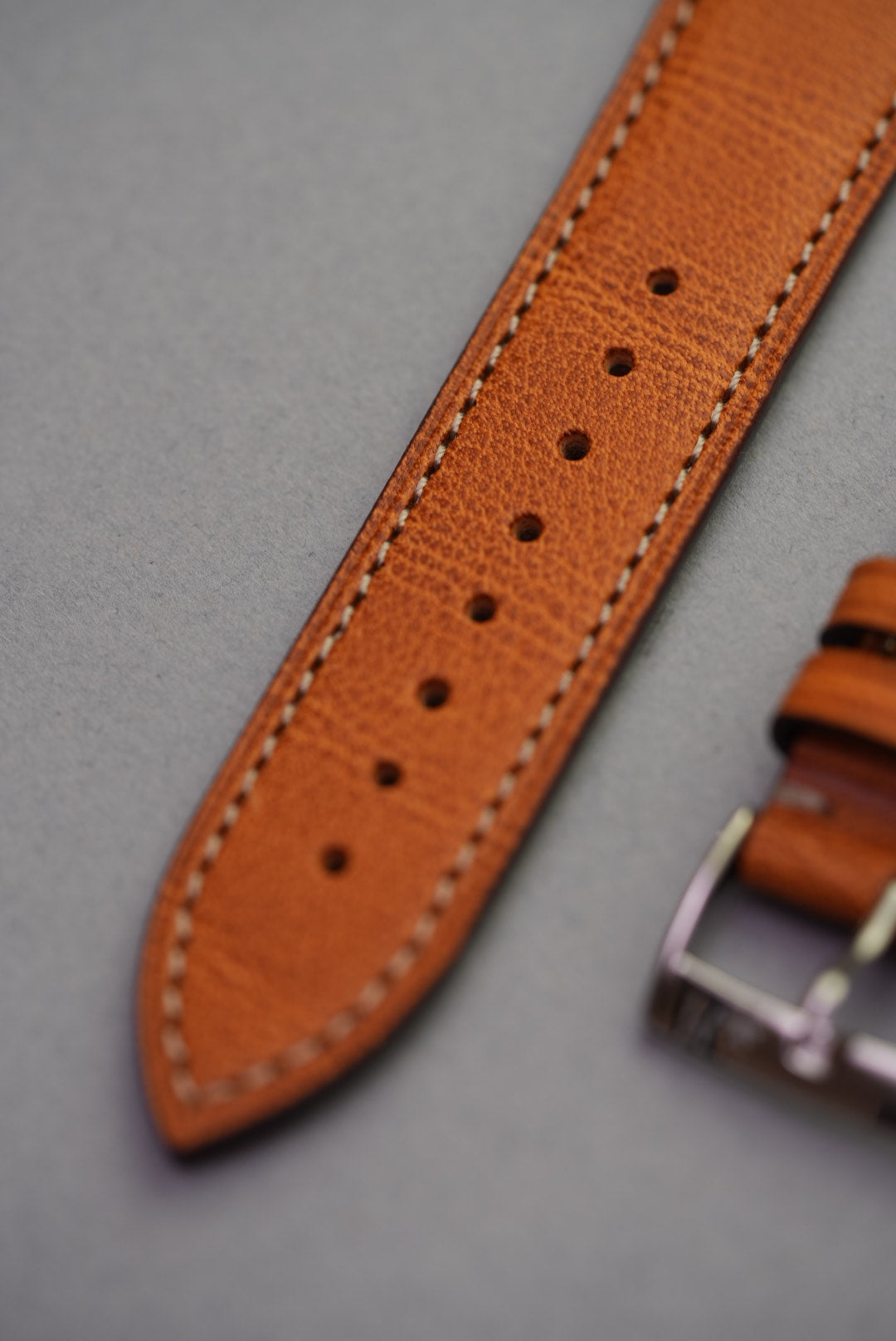 Tapered end of golden brown leather watch strap with stitched edging