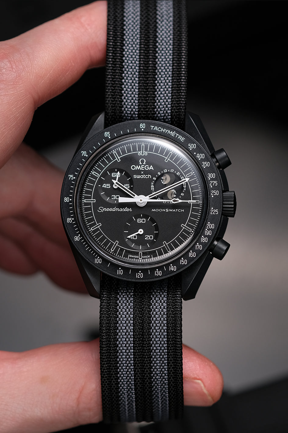 MoonSwatch nylon deployant strap in black and grey — fitted on Snoopy New Moon MoonSwatch, held in hand