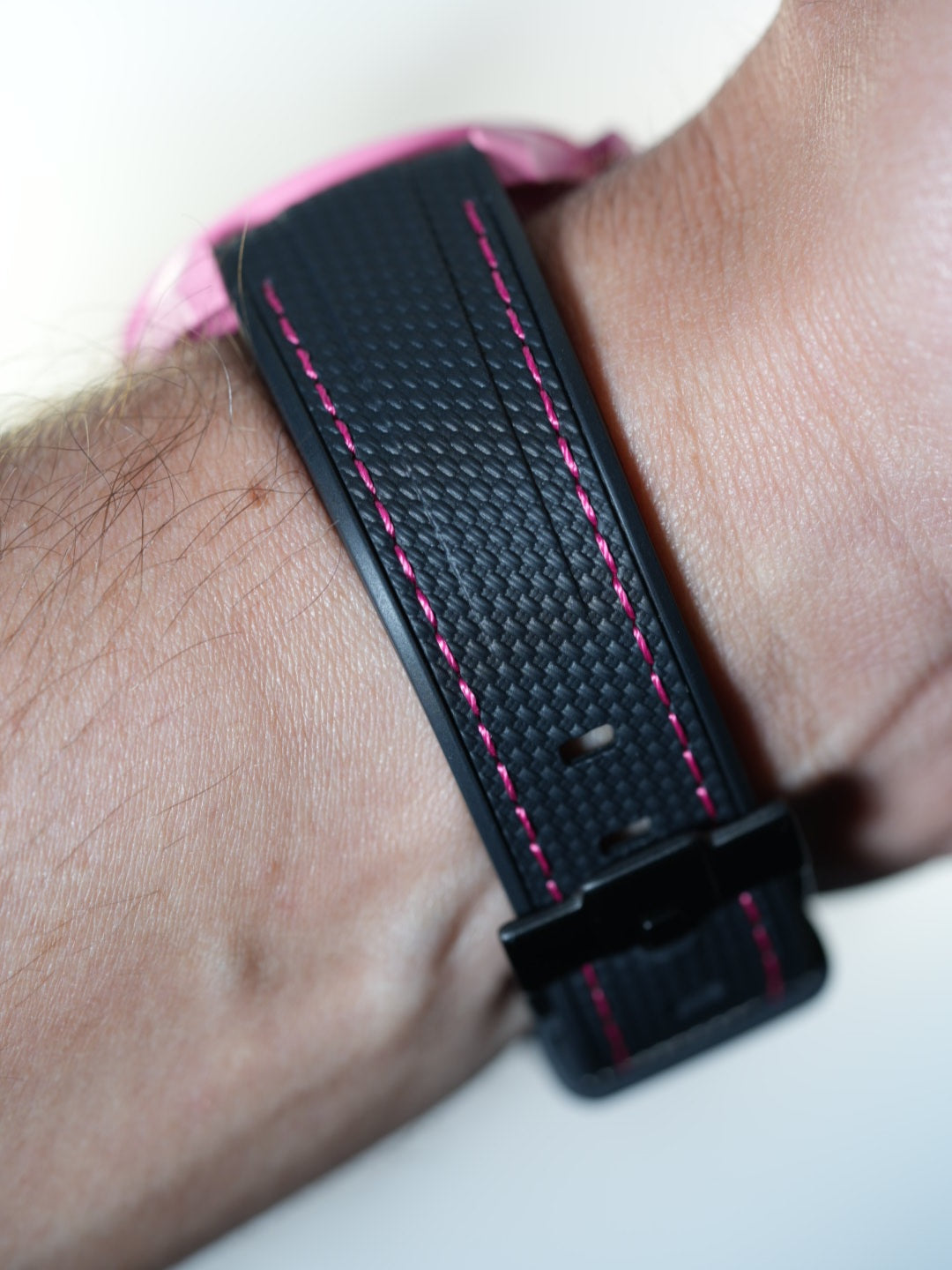 Side wrist view of the MoonSwatch Pink Moonphase paired with black strap and pink stitching – subtle texture and precise fit.