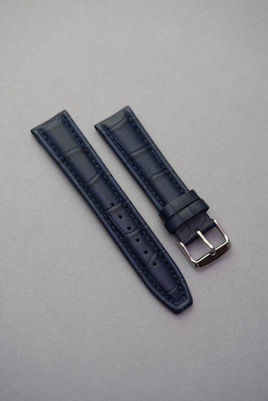 Navy blue alligator-style leather watch strap with matching stitching and polished silver buckle, displayed flat on a light grey background.