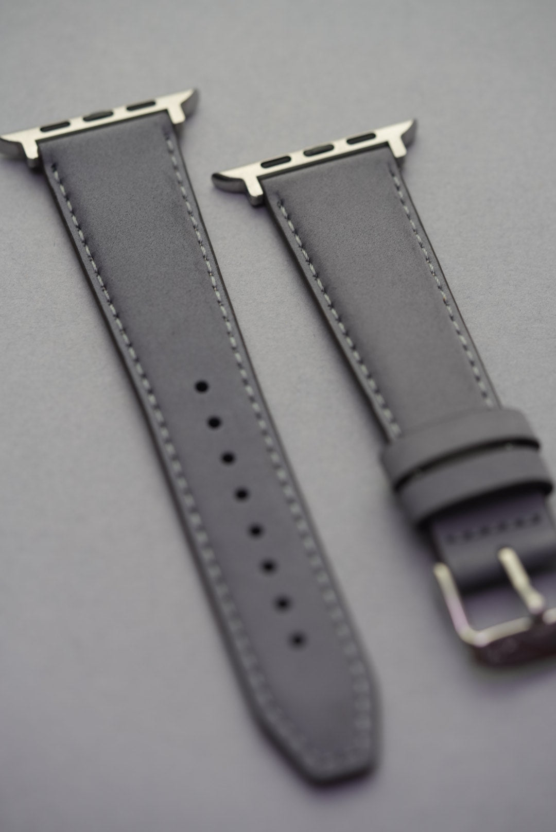 Close-up of grey nubuck strap with Apple Watch adapters, showing soft leather texture and stitching detail.