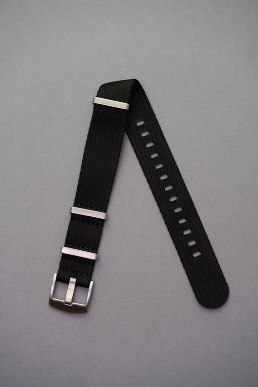 Premium black fabric NATO watch strap with brushed stainless steel keepers, laid flat on grey background.