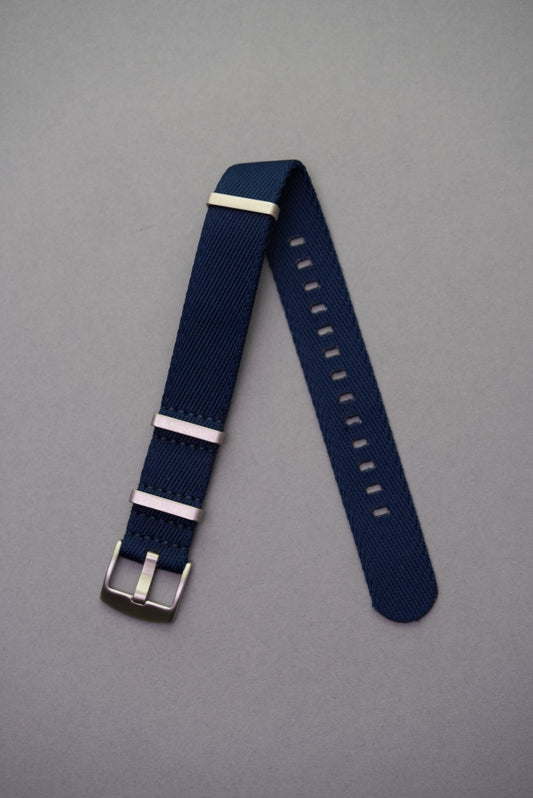 Premium navy fabric NATO watch strap with brushed stainless steel keepers, laid flat on grey background.