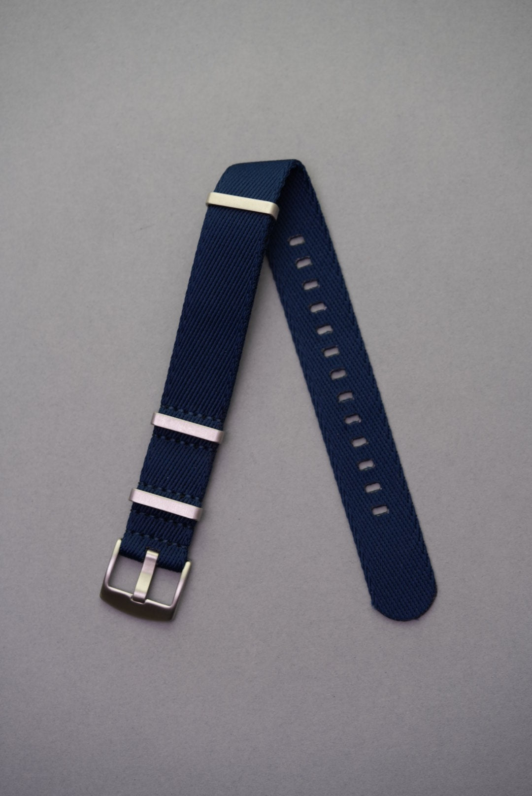 Premium navy fabric NATO watch strap with brushed stainless steel keepers, laid flat on grey background.