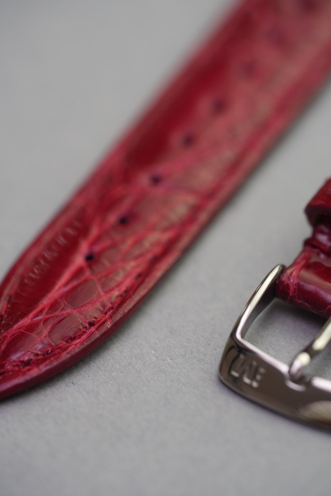 Close-up of the stainless steel buckle and deep grain on ruby crocodile leather watch strap for Cartier timepieces.
