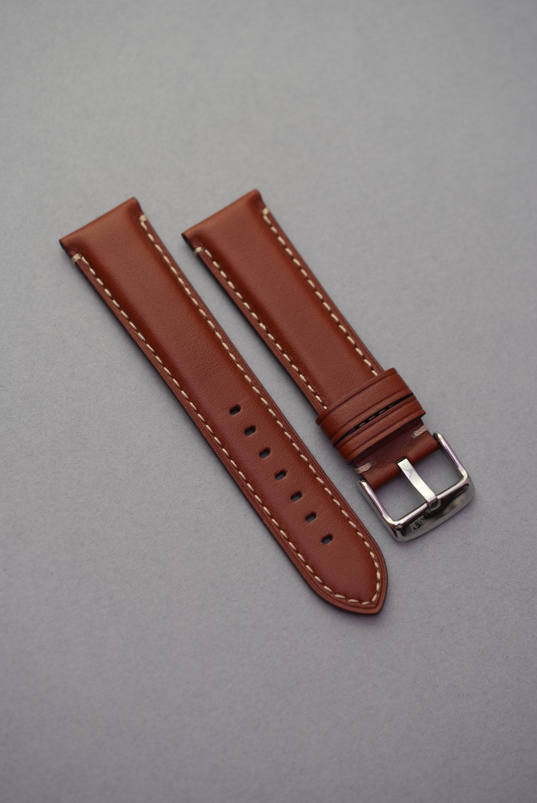 Tan leather watch strap with cream contrast stitching laid flat for strap replacement