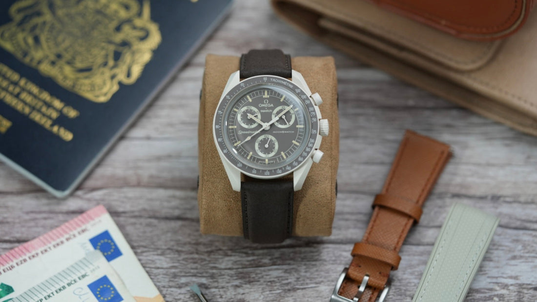 Swatch X OMEGA MoonSwatch Mission On Earth Desert on a Nubuck leather strap, displayed on a suede watch cushion. Surrounded by a UK passport, Euro banknotes, and additional watch straps, evoking a stylish travel theme.