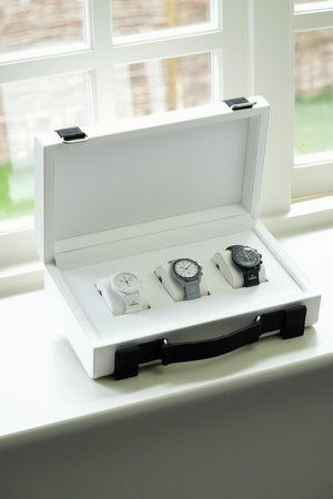 Three MoonSwatch watches in a white display case on a windowsill.