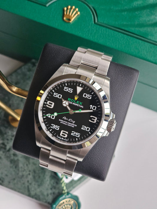 Rolex AirKing watch 126900, on a watch stand, time showing ten past ten. Watch angled to the right. Part of the green rolex box showing in the background