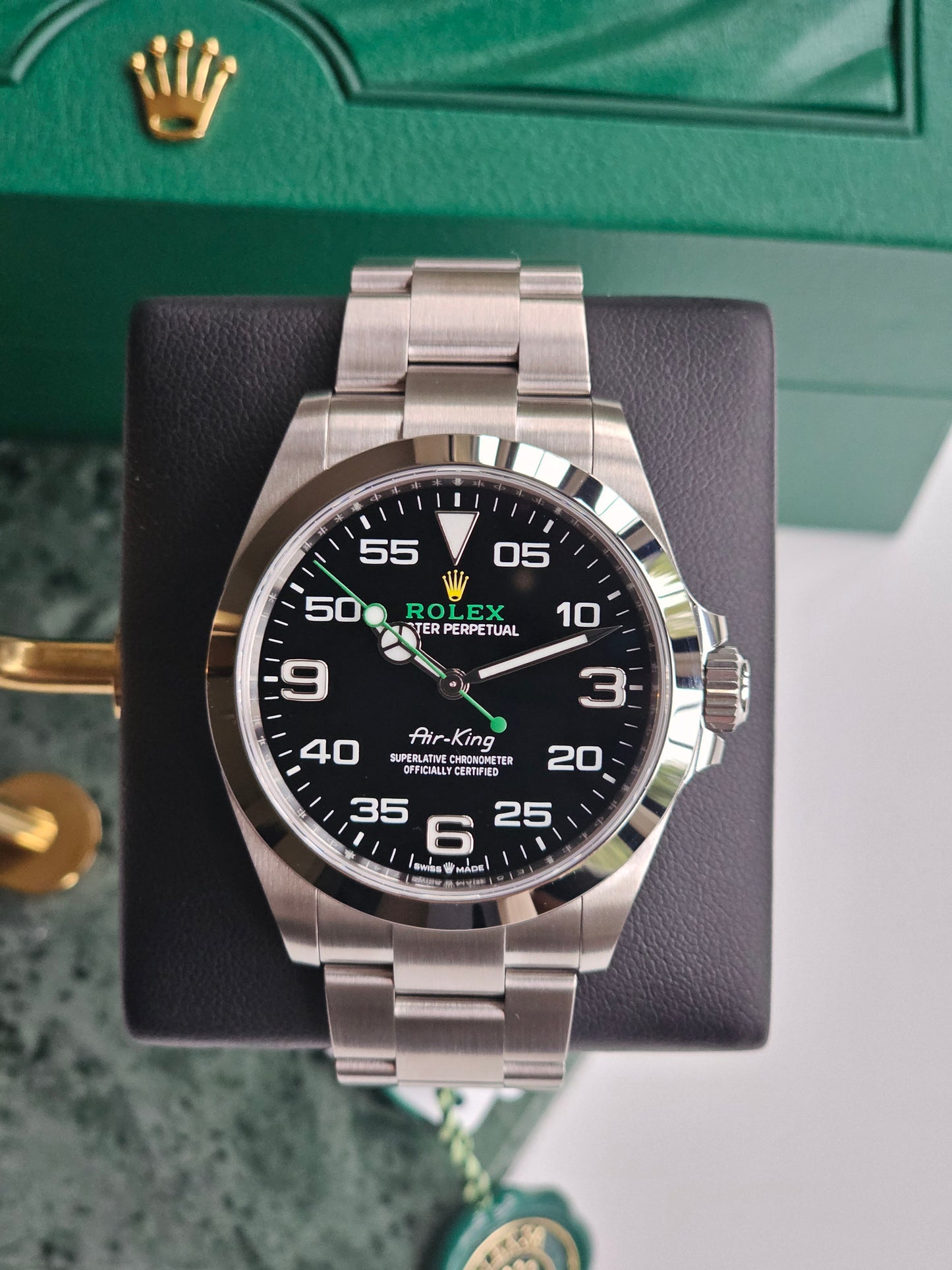 Rolex AirKing watch 126900, on a watch stand, time showing ten past ten. Watch angled straight on. Part of the green rolex box showing in the background