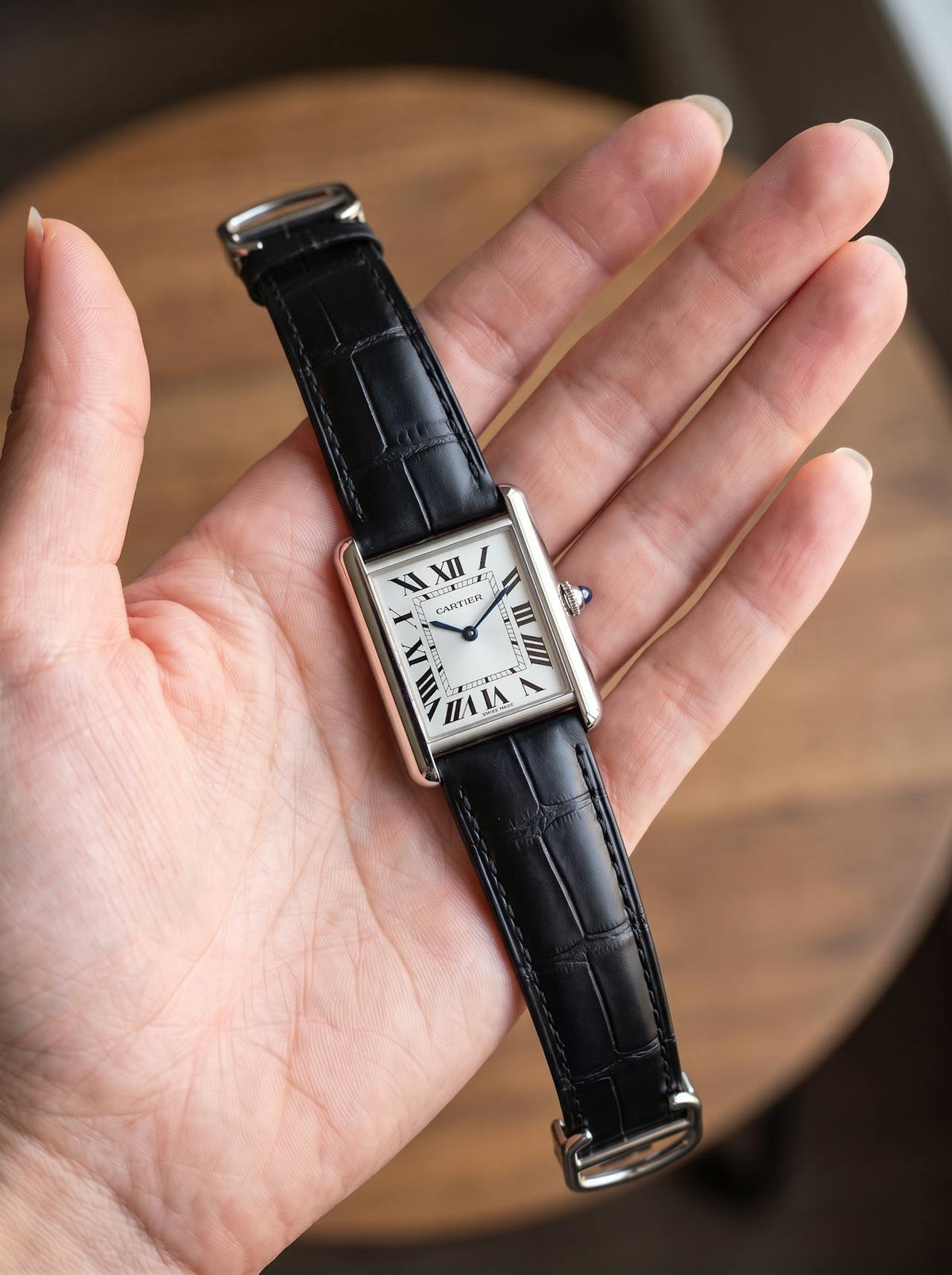 Cartier Tank Must Small on a black square alligator-grain leather strap, held in hand