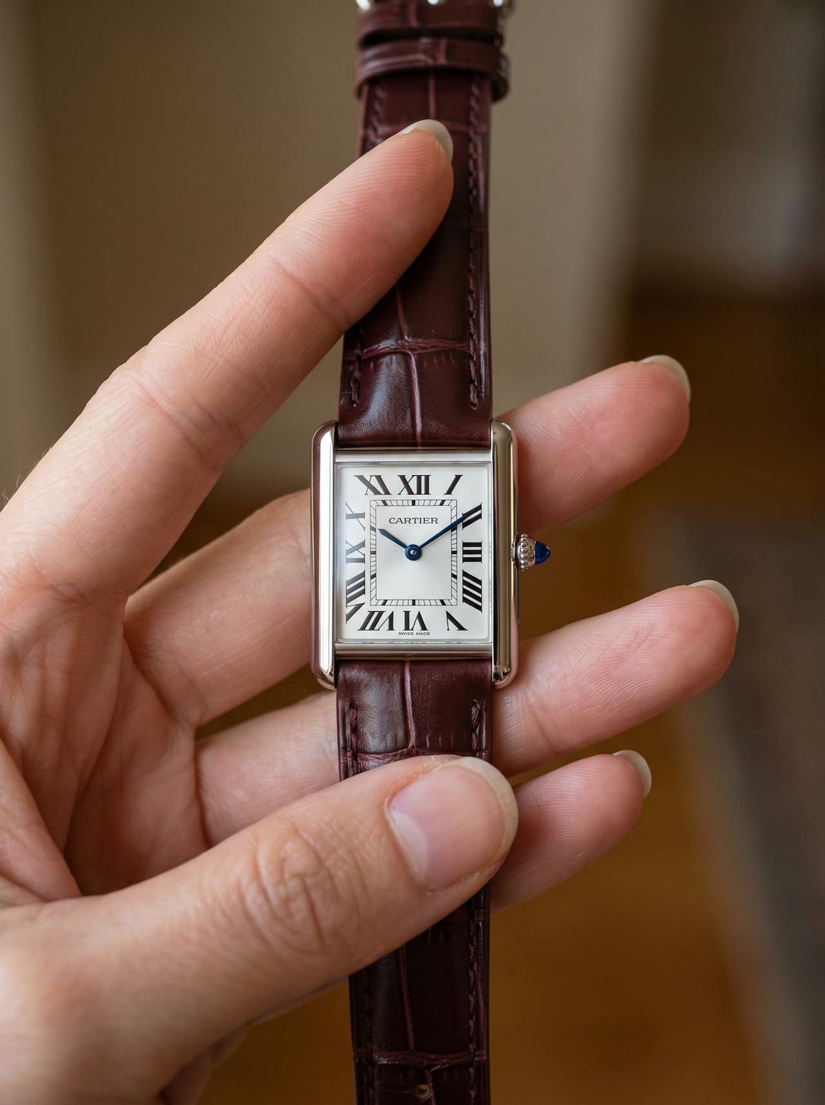Cartier Tank Must Small on a brown square alligator-grain leather strap, held in hand