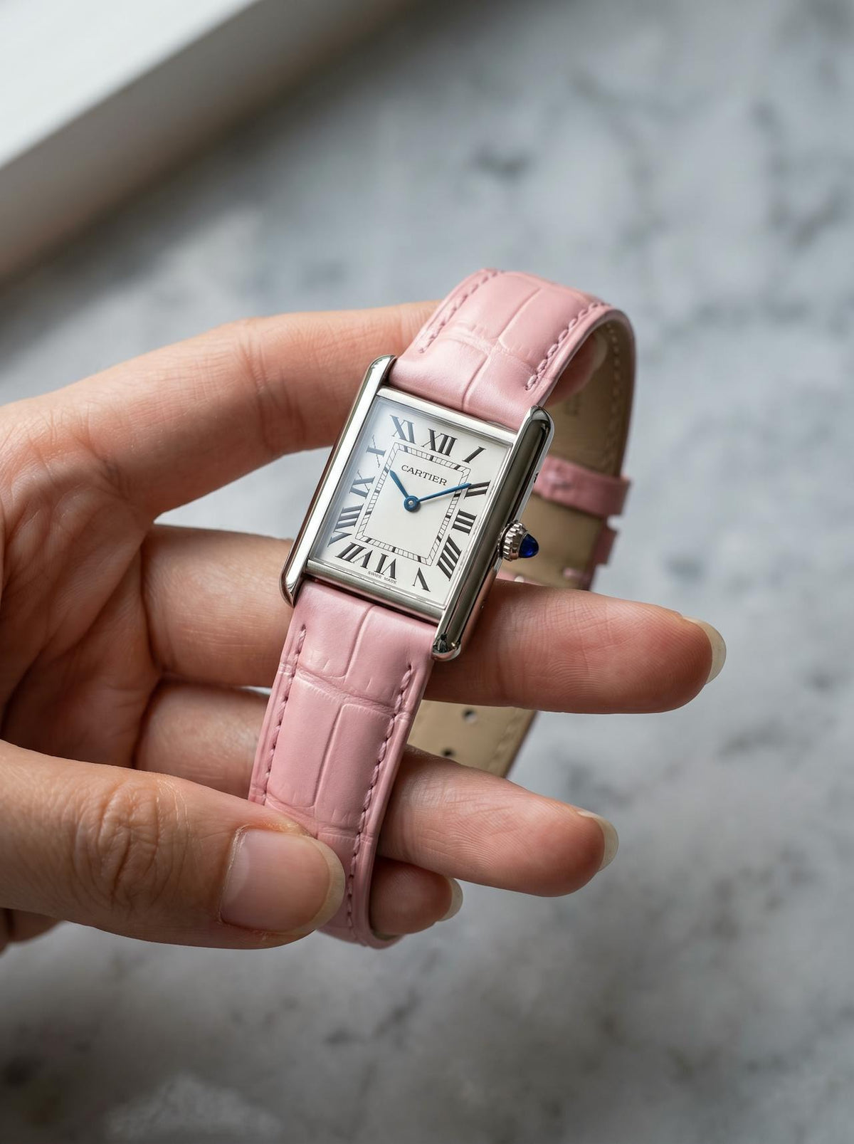 Cartier Tank Must Small on a pink square alligator-grain leather strap, held in hand