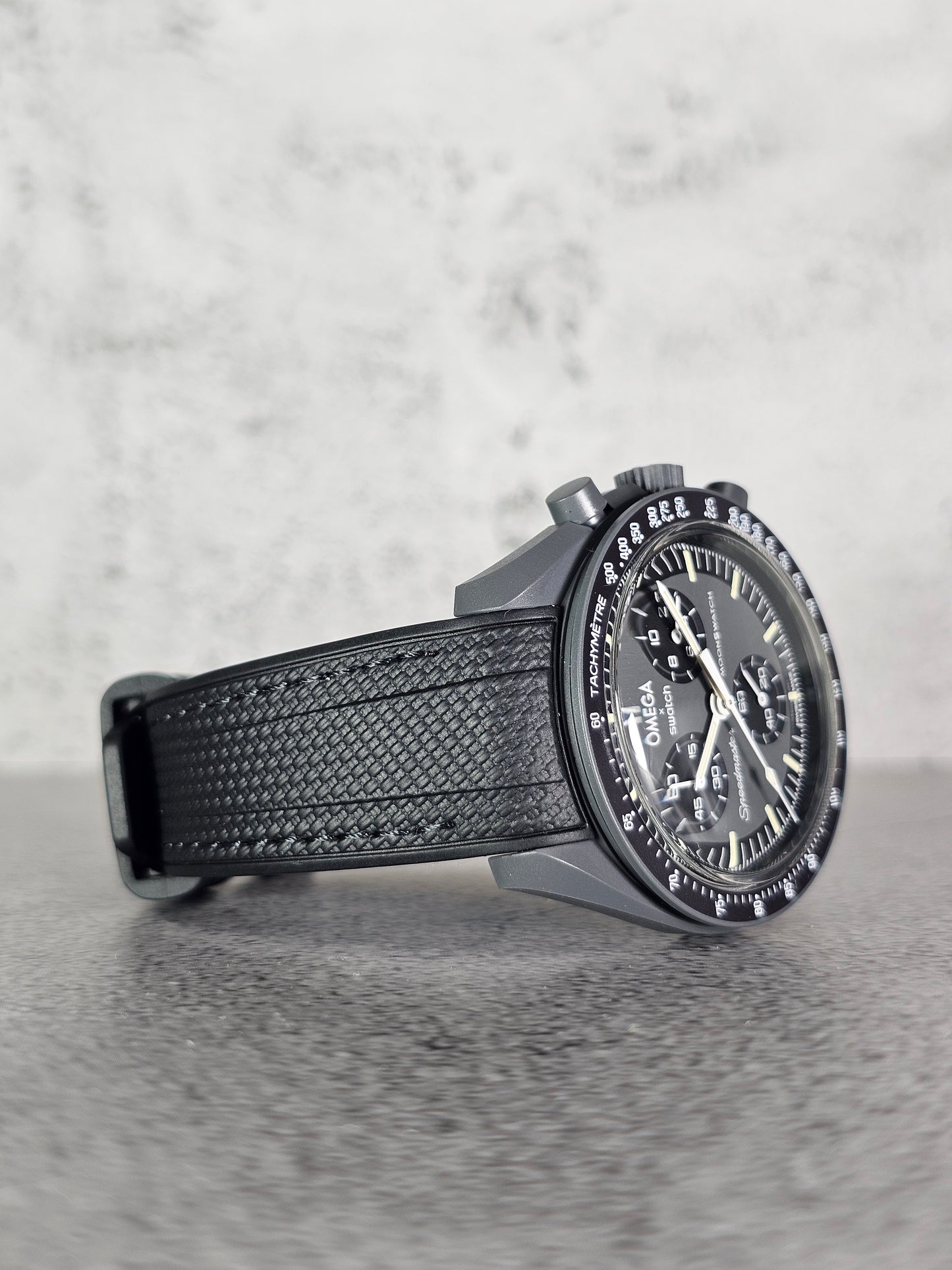 A black stitched rubber woven strap with a curved edge, designed for a watch with a 20mm lug width, displayed on a grey textured background.