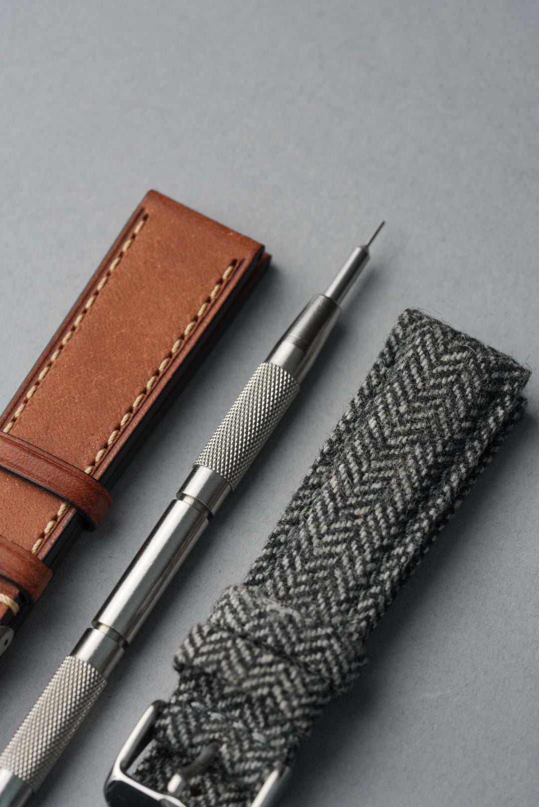 Silver pen with brown leather case and gray herringbone fabric on a gray background