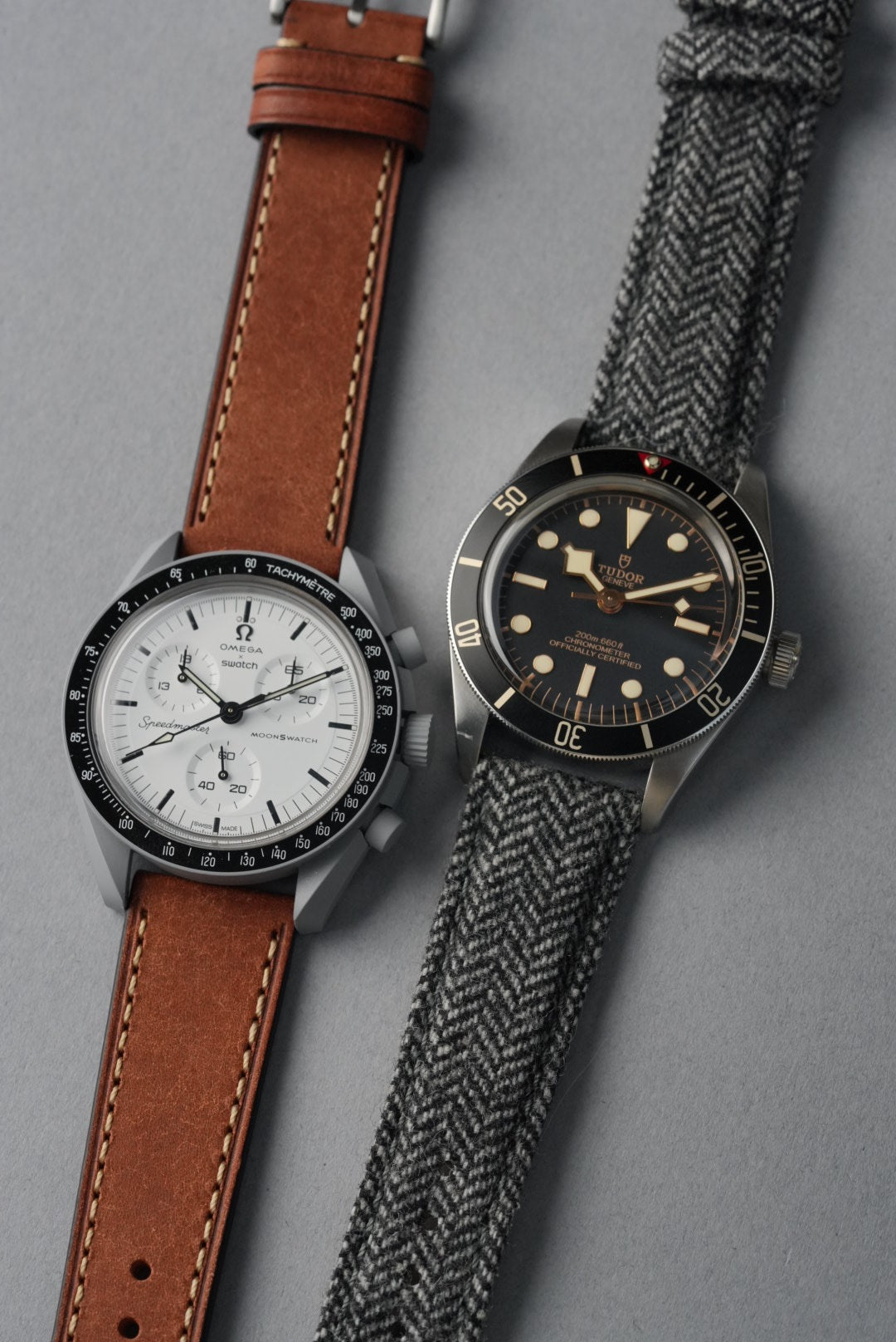 Two watches with brown leather strap and gray textured strap on a gray background