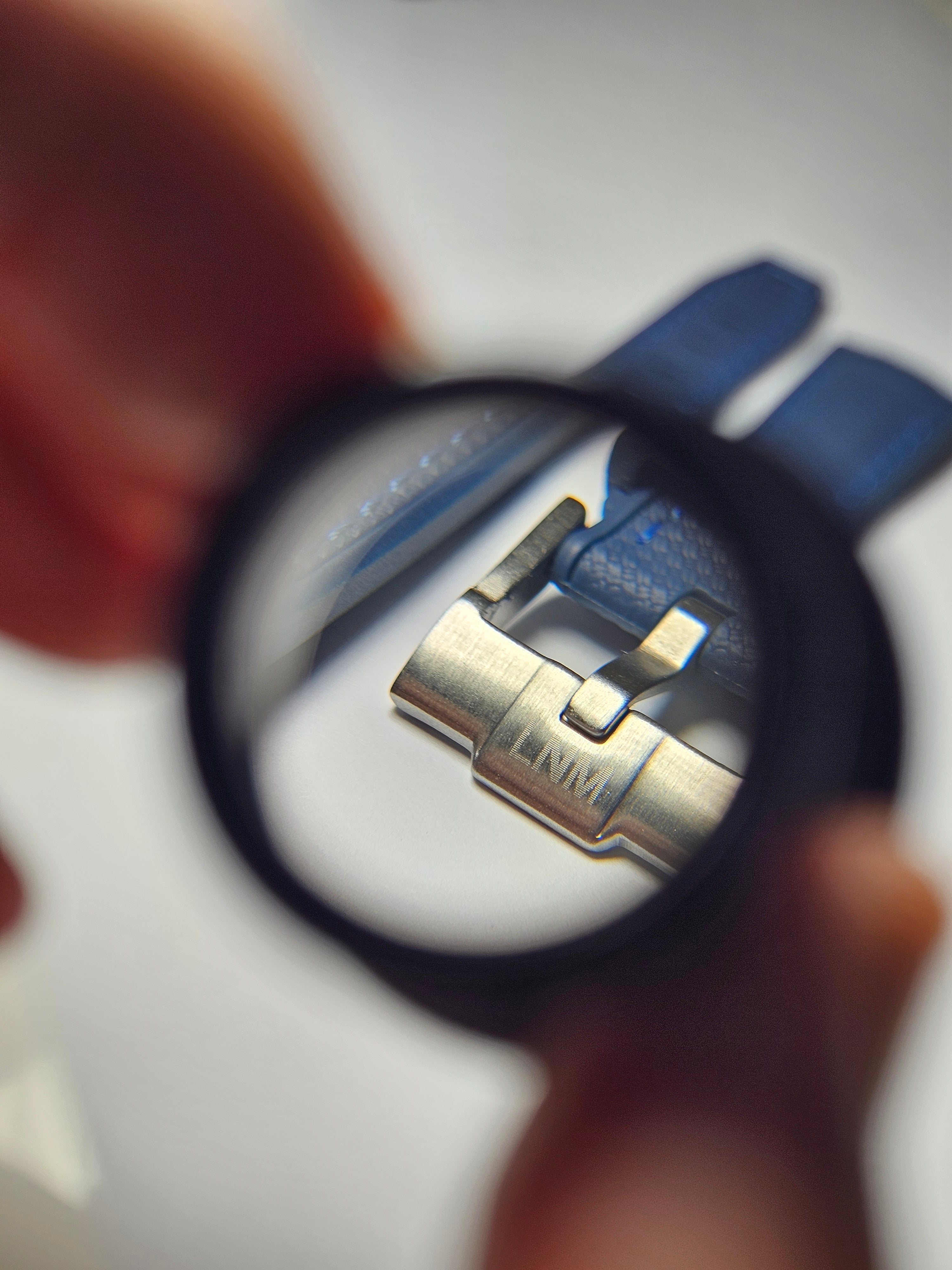 A close-up of a rubber watch strap buckle with engraved text on it, viewed through a magnifying glass.