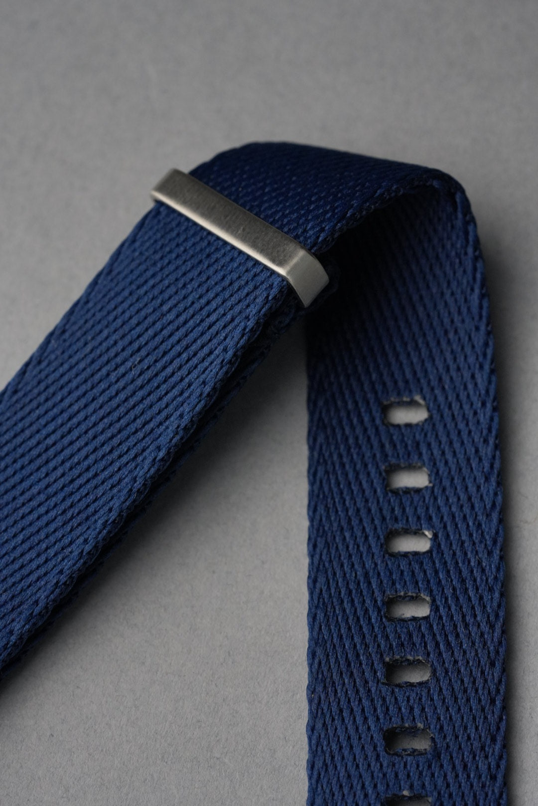 Blue woven watch strap with silver buckle on a gray background