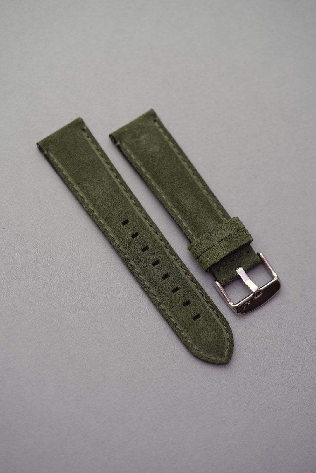 Green suede leather watch strap laid flat with stainless buckle for strap replacement