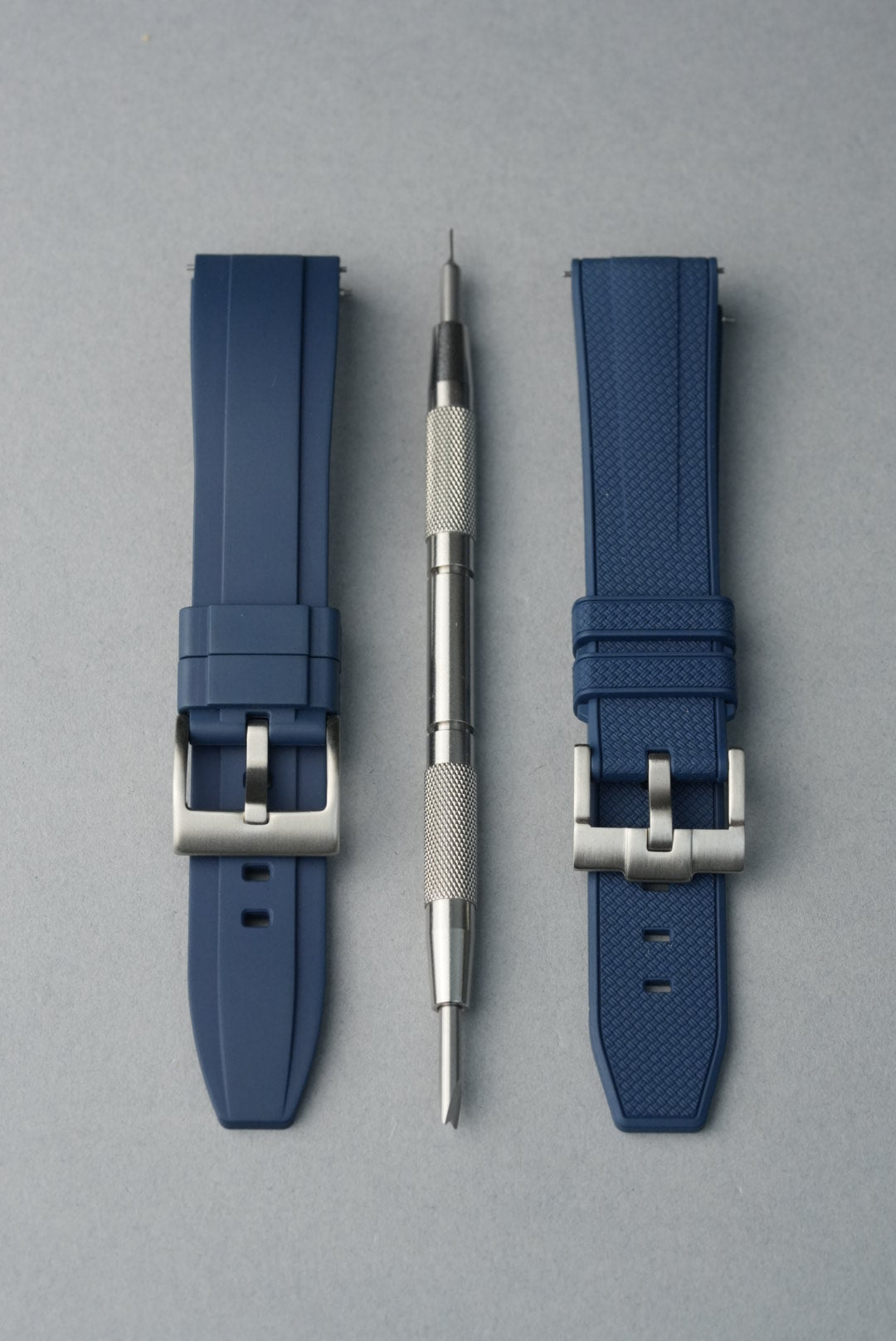 Two blue watch straps with silver buckles and tools on a gray background