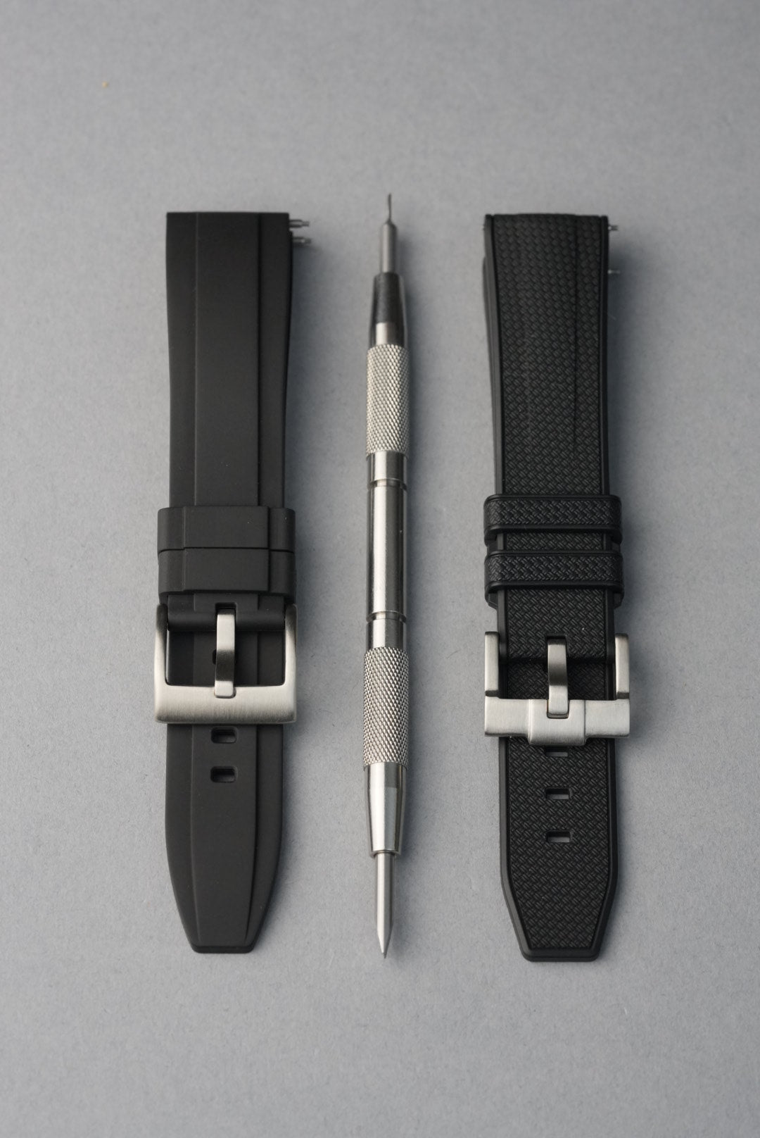 Two black watch straps with silver buckles on a gray background