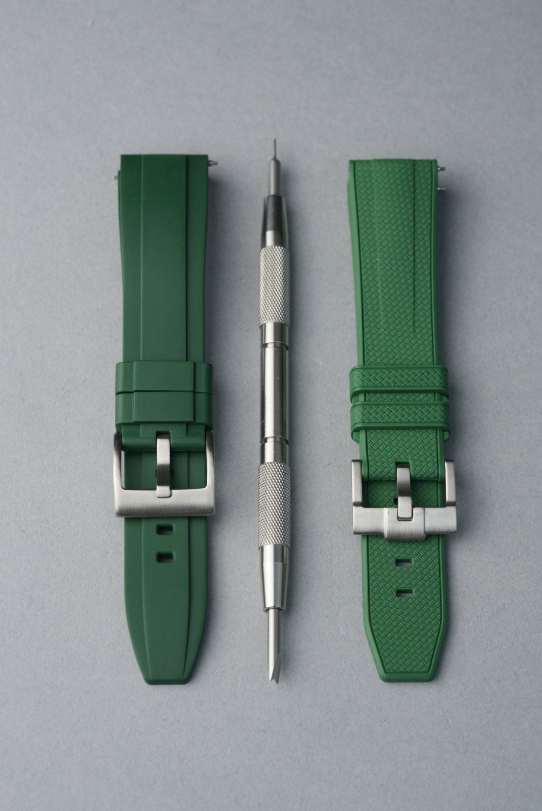 Two green watch straps with silver buckles and a tool on a gray background