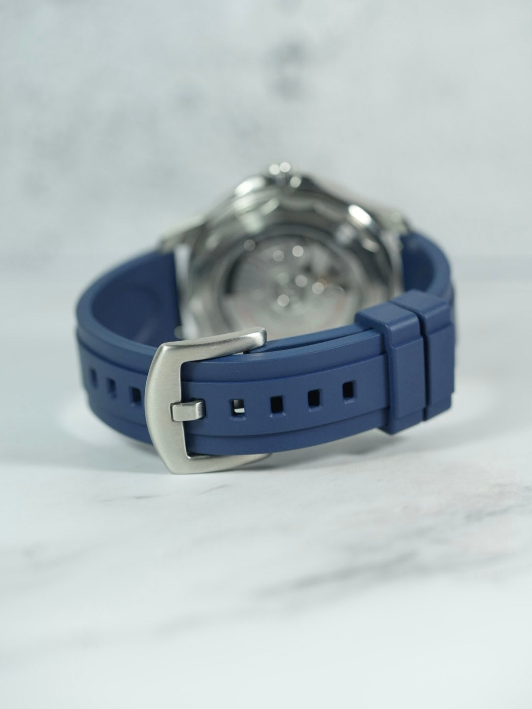 Rear view of the Omega Seamaster, focusing on the polished buckle and strap detailing against a marble backdrop. Navy Strap