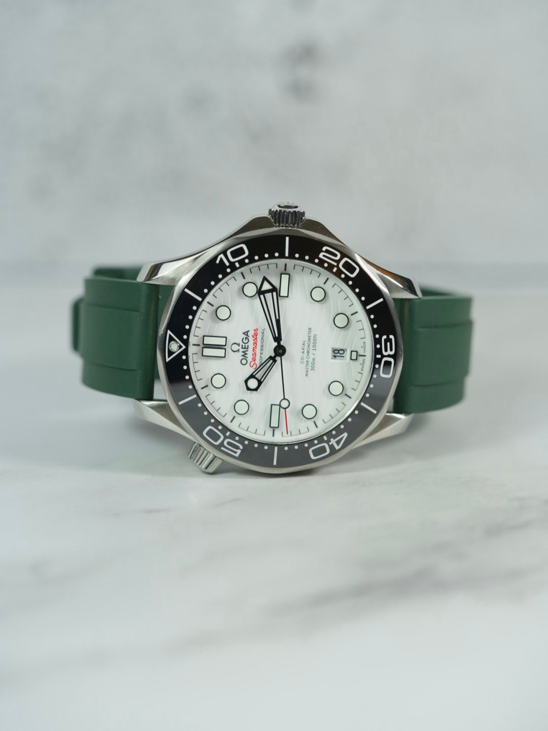 Front view of an Omega Seamaster watch with a GREEN FKM rubber strap, showcasing its sleek design on a marble background.