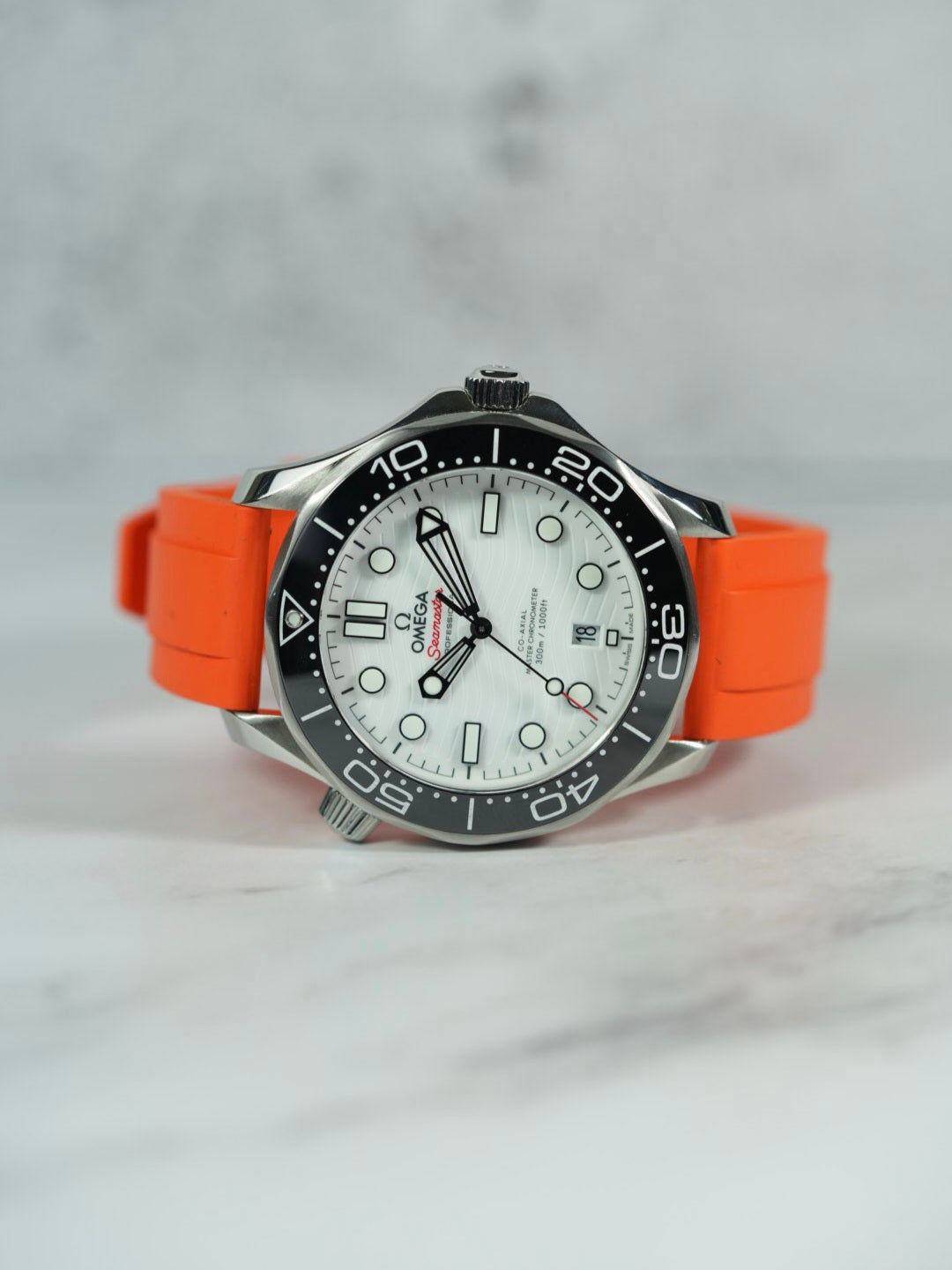 Front view of an Omega Seamaster watch with a ORANGE FKM rubber strap, showcasing its sleek design on a marble background.