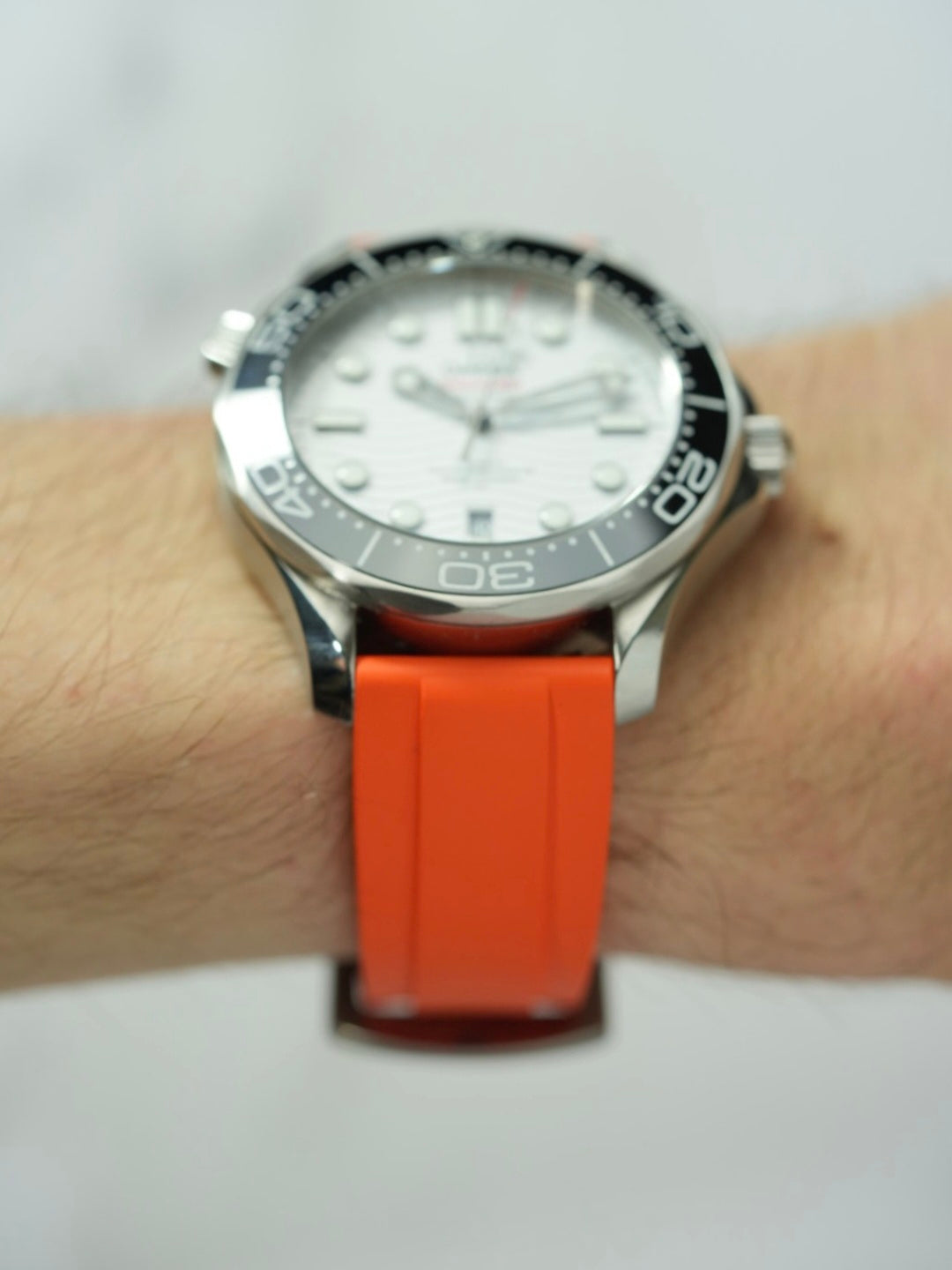 Wrist view of the Omega Seamaster, featuring the elegant orange FKM rubber strap and the watch's detailed dial design.