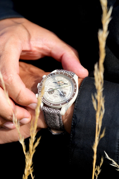Close-up of a hand wearing a detailed wristwatch with a textured strap, set against a dark background.