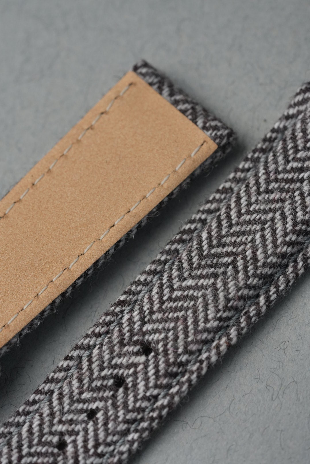Close-up of a herringbone patterned strap with a brown leather patch on a gray background