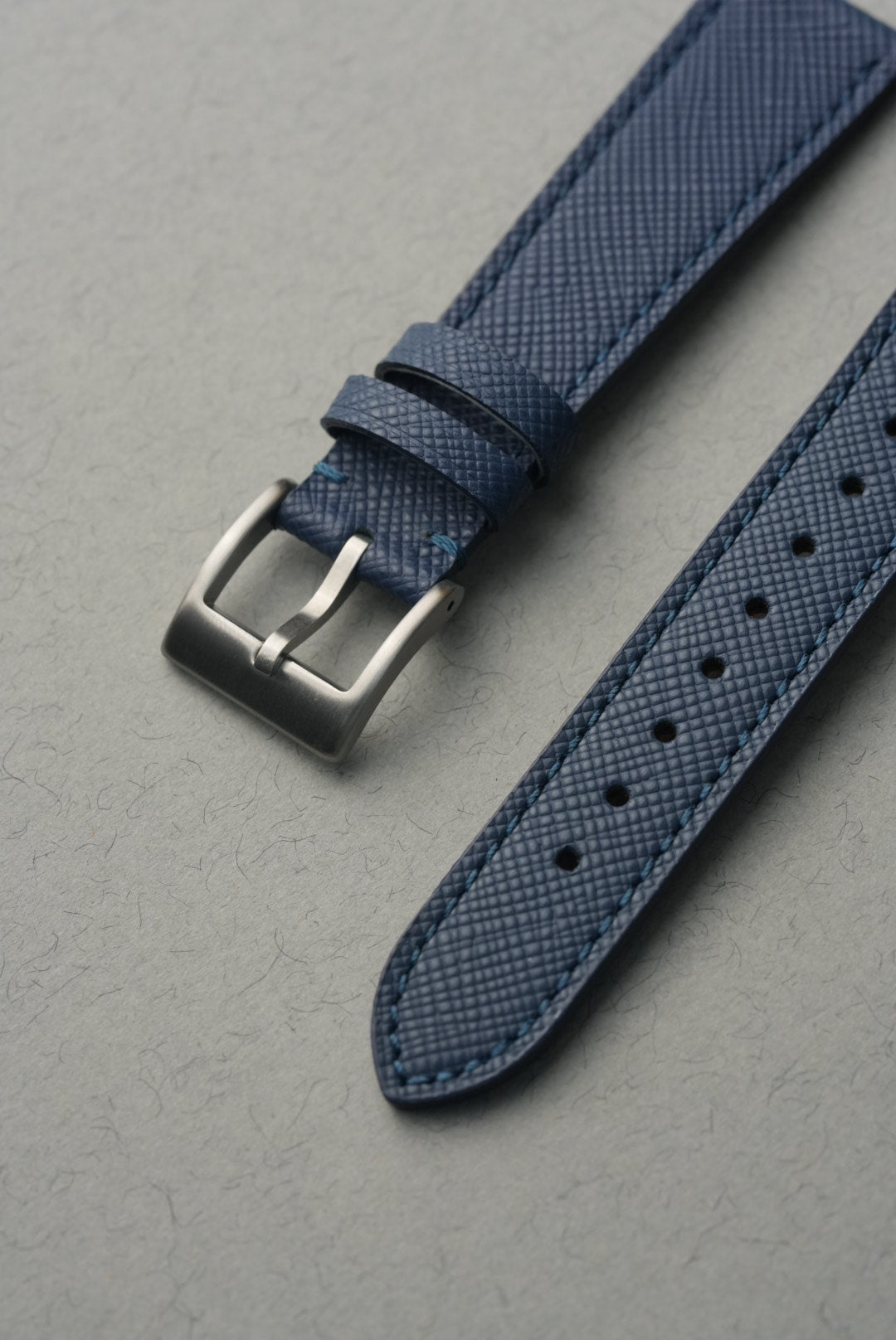 Blue textured watch strap with silver buckle on a gray background