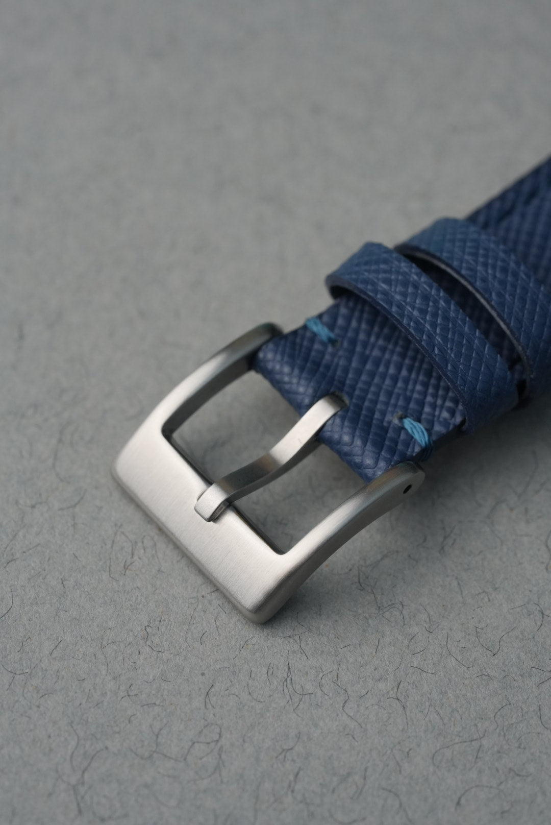 Blue woven strap with a silver buckle on a gray background
