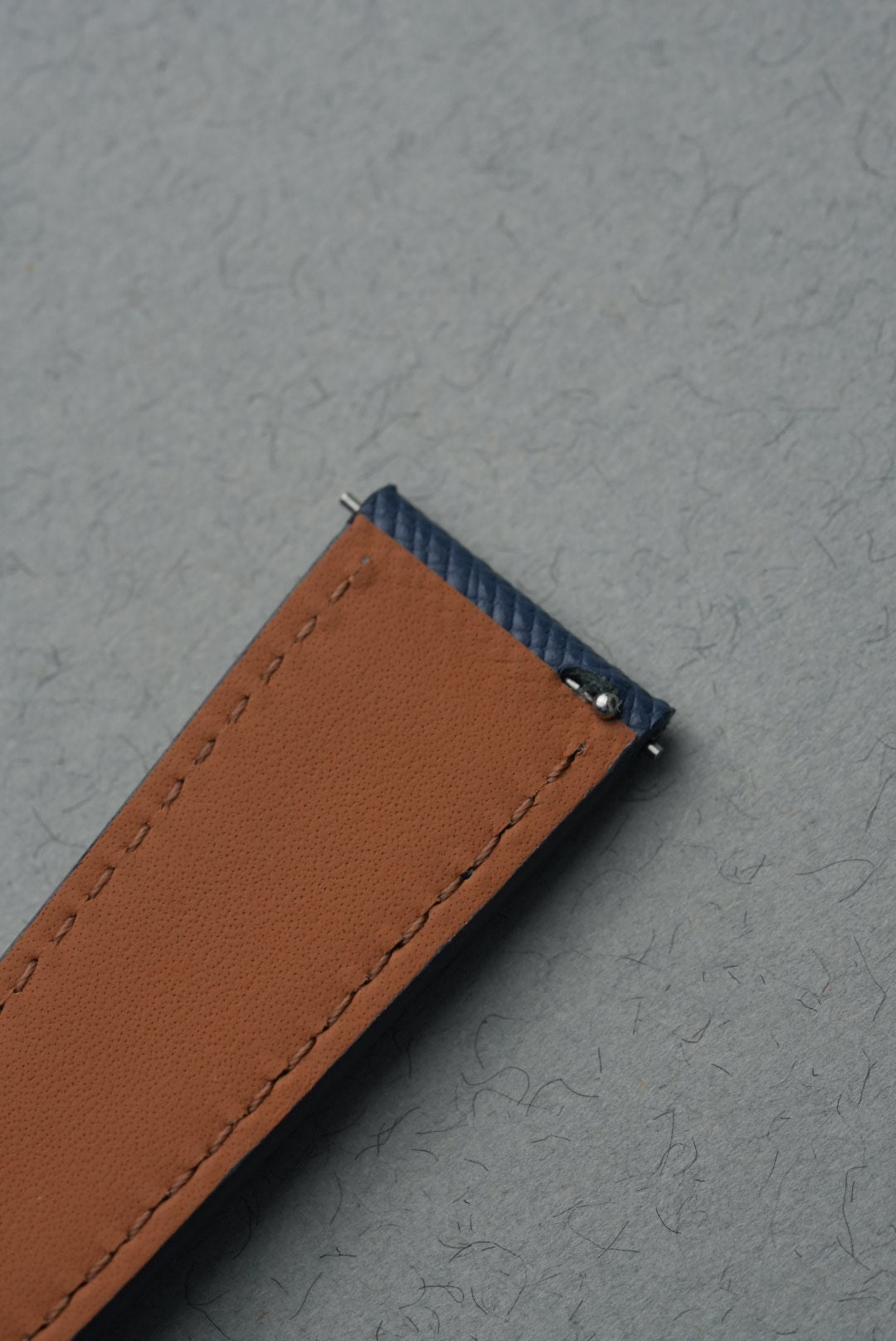 Close-up of a brown leather strap with stitching on a gray background