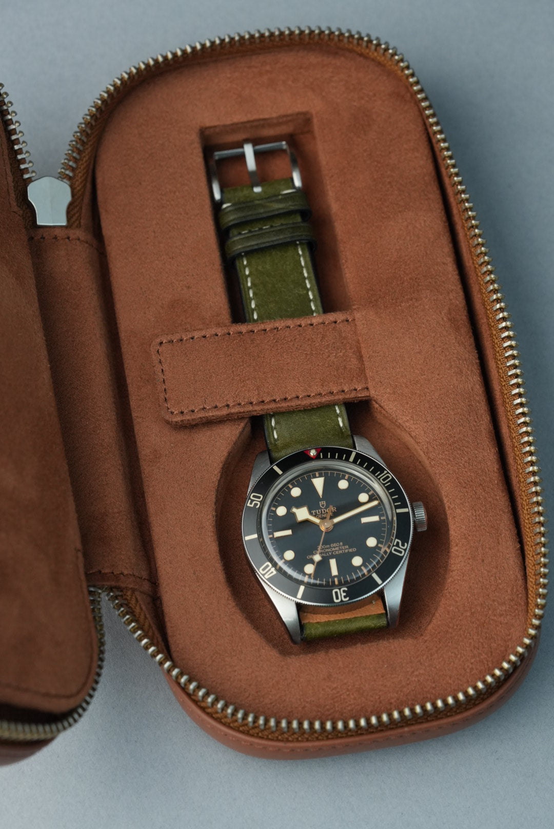 Watch with a green strap in an open brown leather case on a gray background