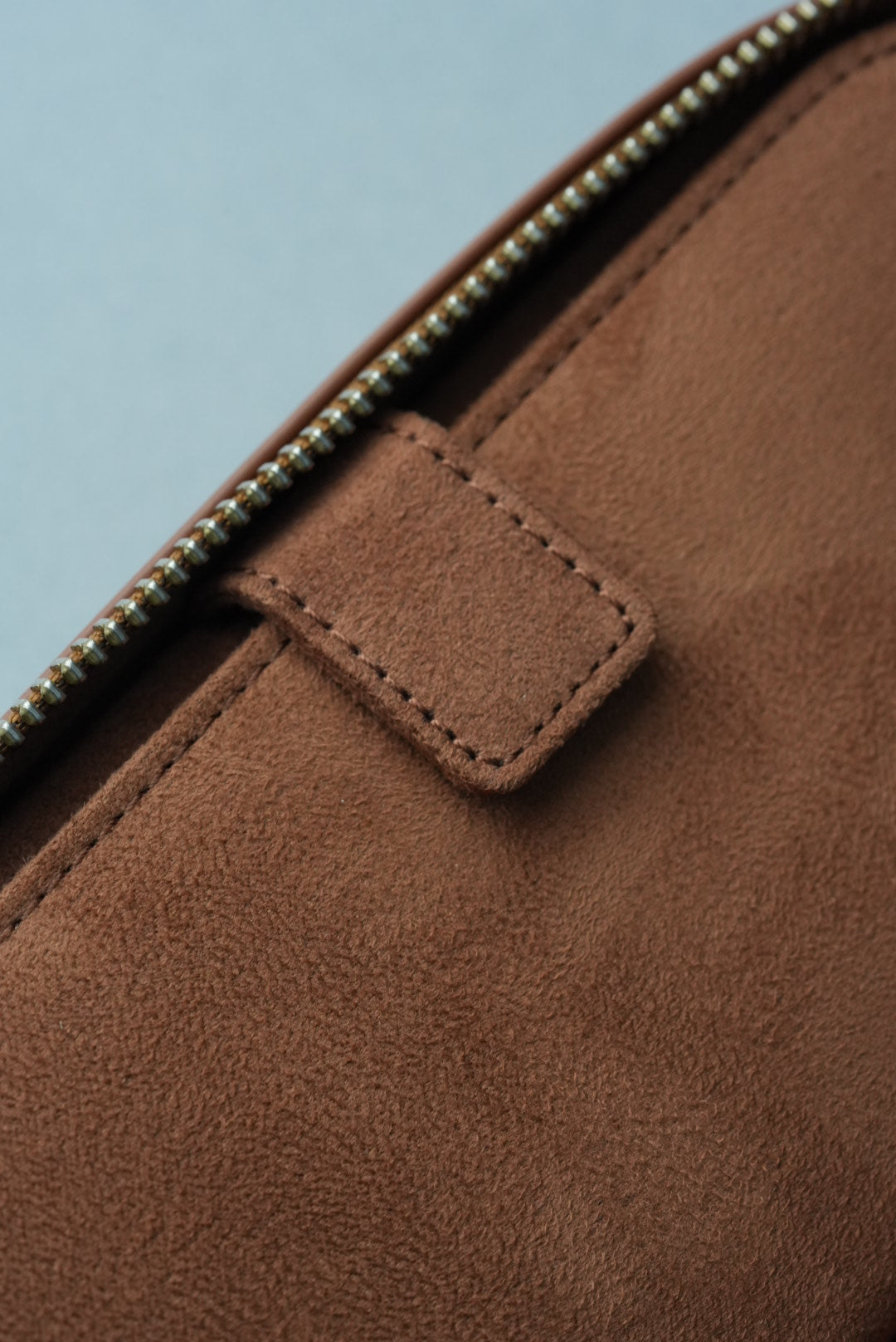 Close-up of a brown suede bag with a zipper on a light blue background
