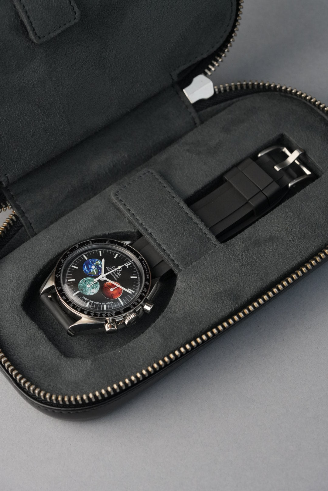 Black watch with colorful face and additional strap in a gray case on a light gray background